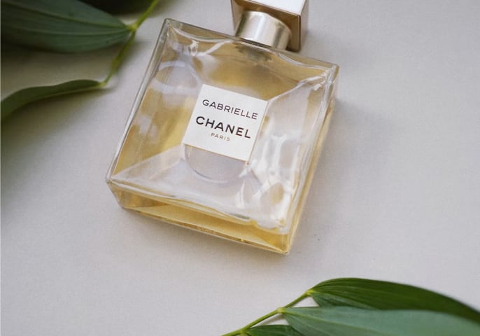 A bottle of Gabrielle Chanel perfume, with a square, clear glass design and a metallic cap.